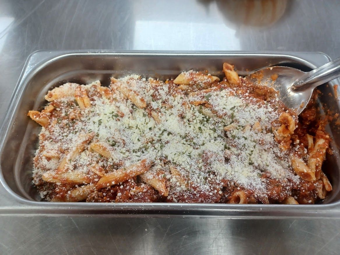 Pasta in red sauce topped with grated cheese in a metal serving tray.