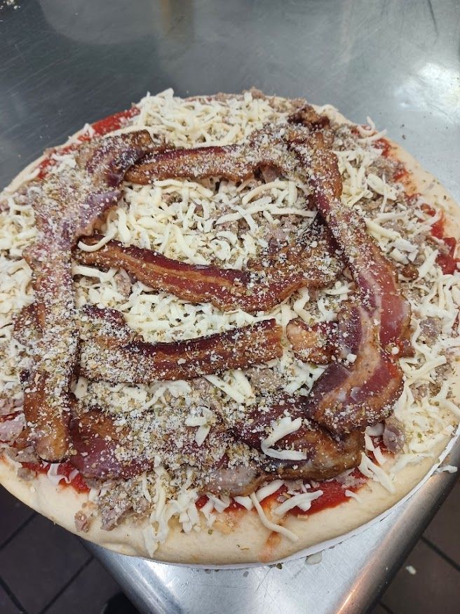 Uncooked pizza topped with bacon, sausage, and shredded cheese.
