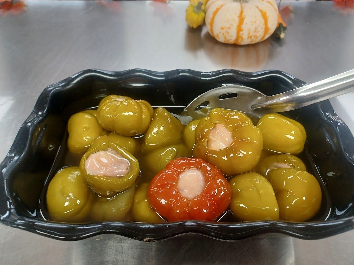 Green pickled tomatoes in a black container, with a serving spoon. One red tomato is also in the container.