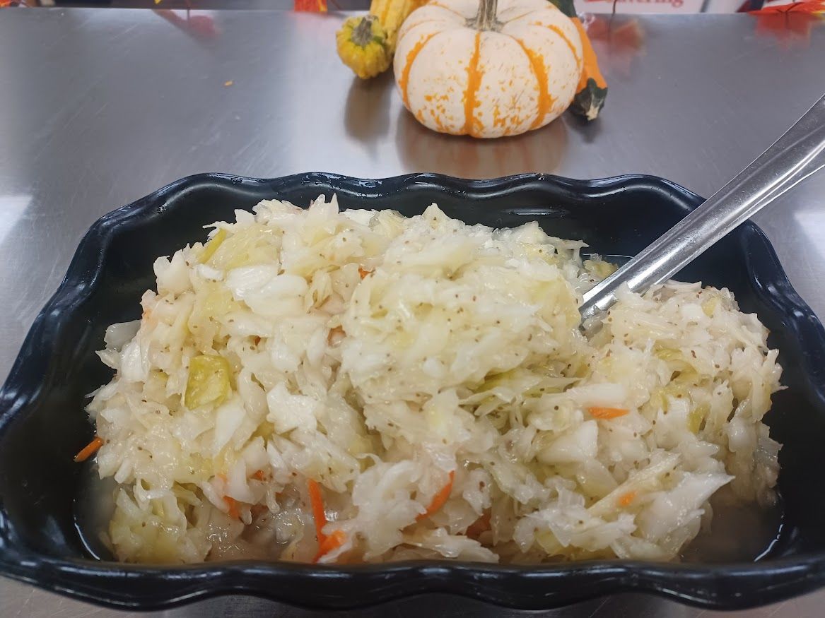 Sauerkraut in a black dish, silver serving spoon, small pumpkins in background.