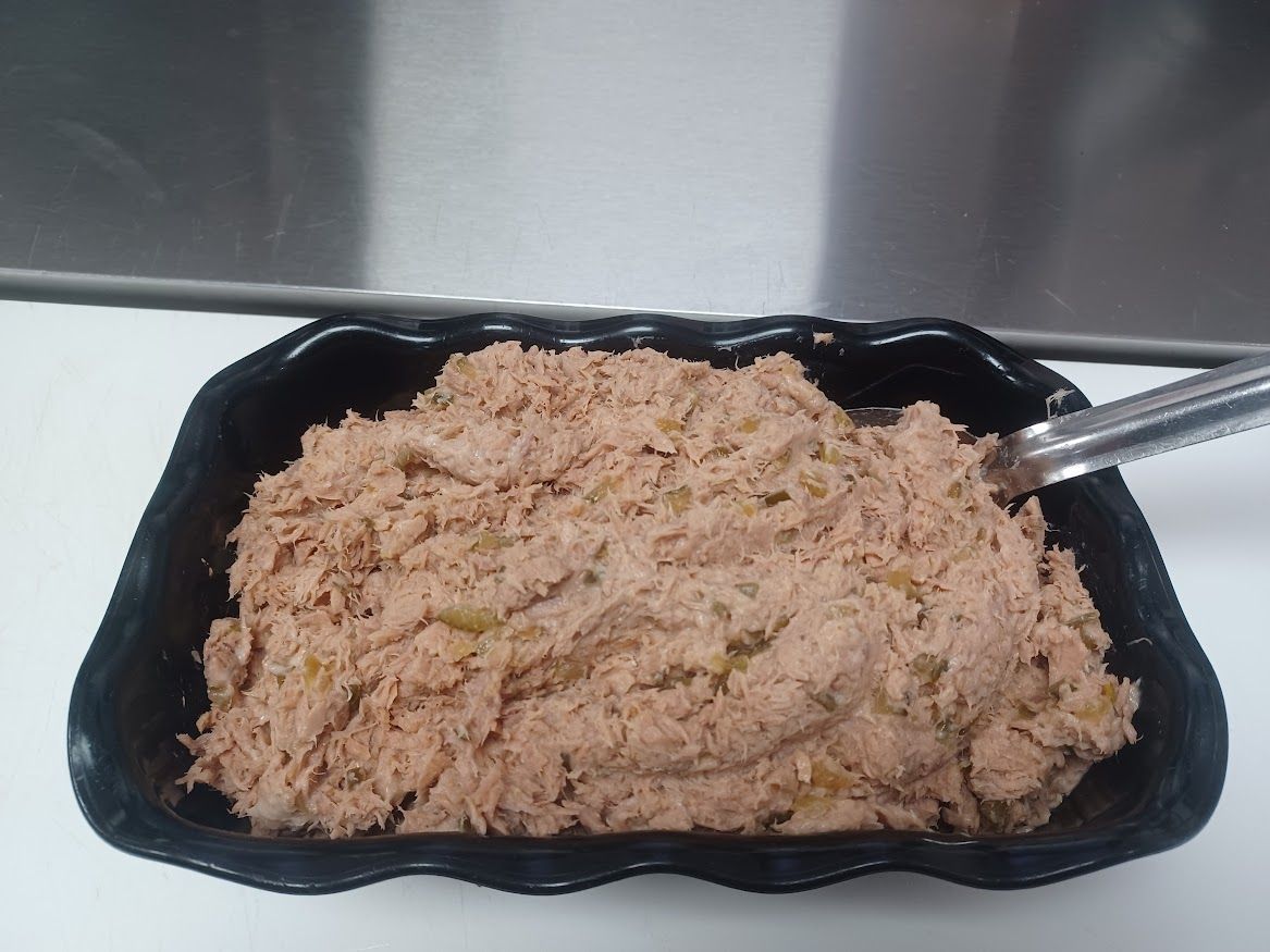 A black bowl of mashed, brown food, possibly tuna, with metal tongs.