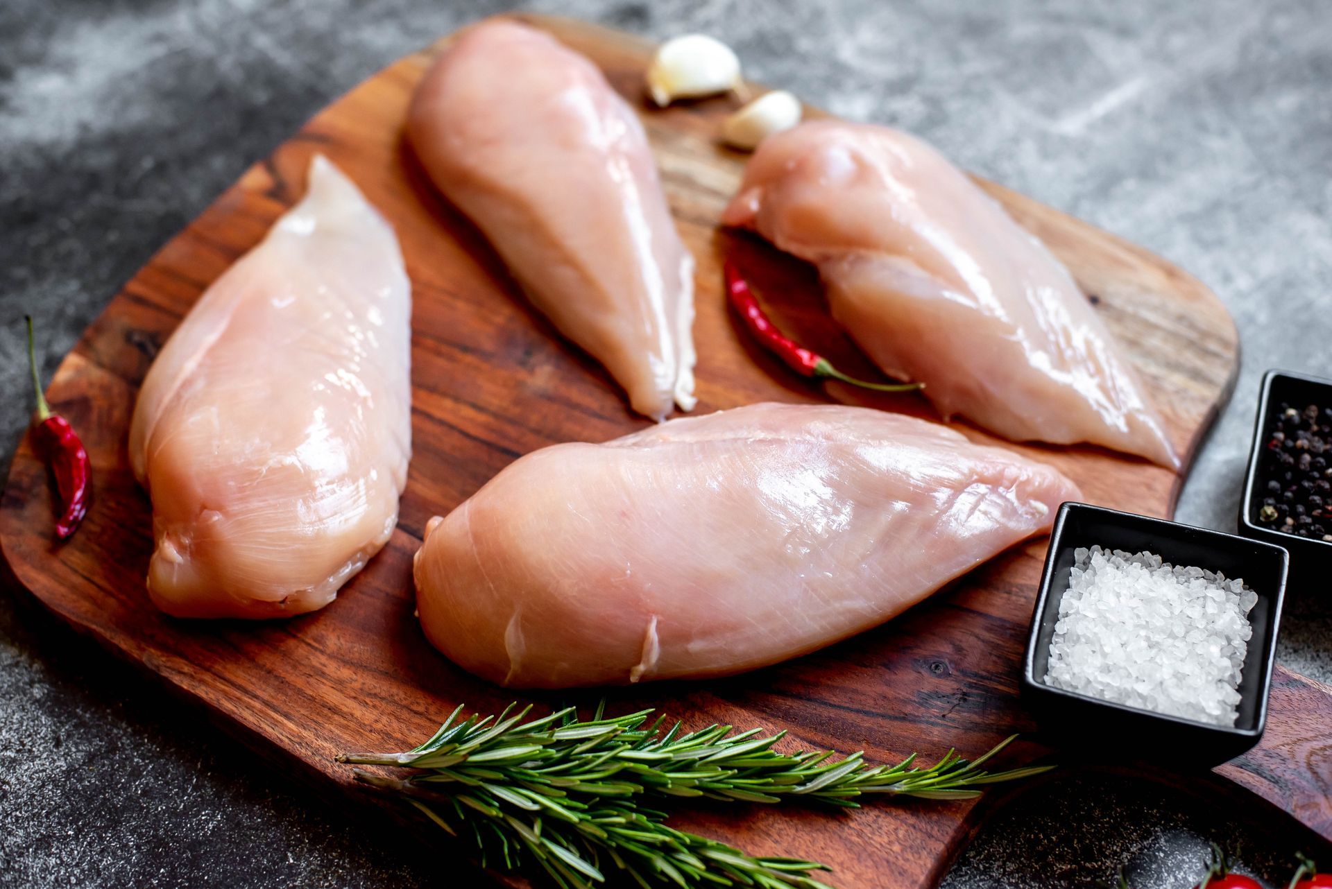 Raw chicken breasts on a wooden cutting board with seasonings and herbs.