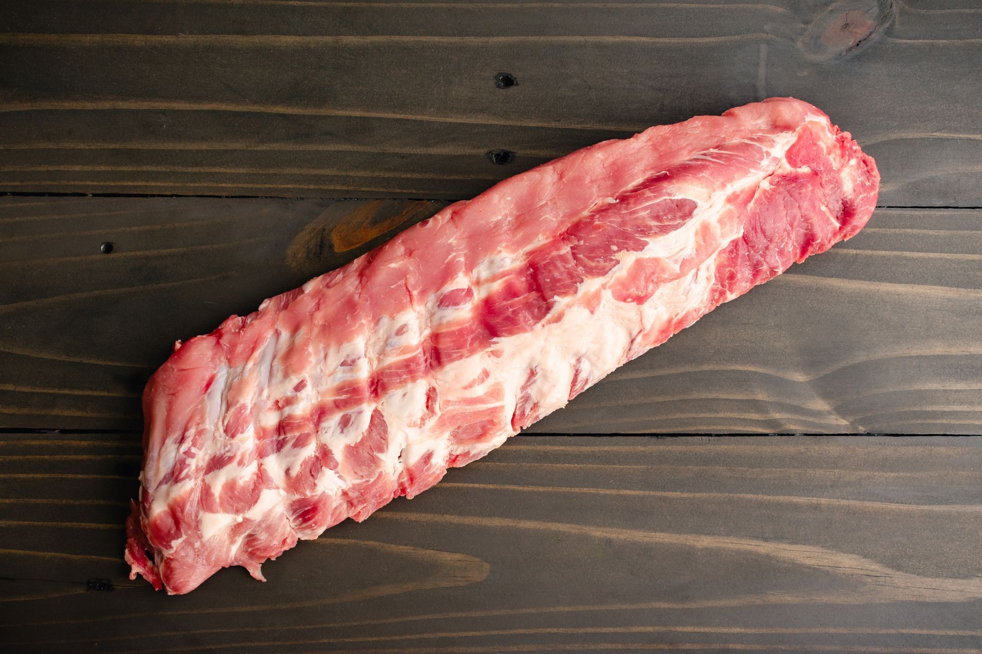 Raw pork ribs on a dark wooden surface.