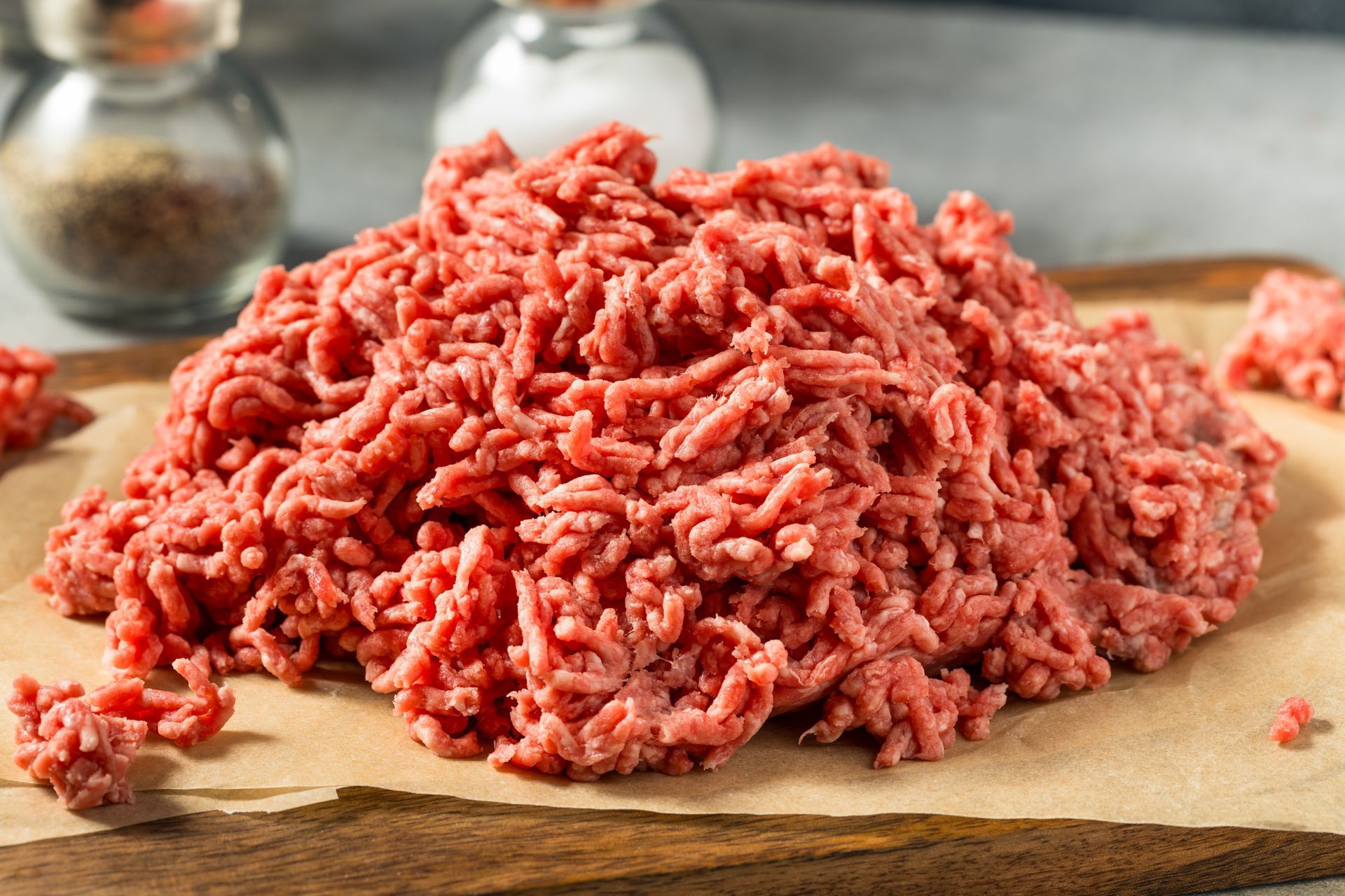 Raw ground beef on a cutting board, with salt and pepper shakers in the background.