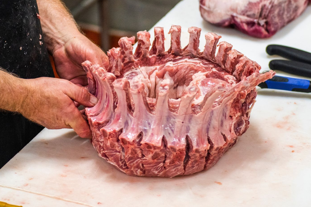 Butcher holding a raw crown roast of pork on a white cutting board.