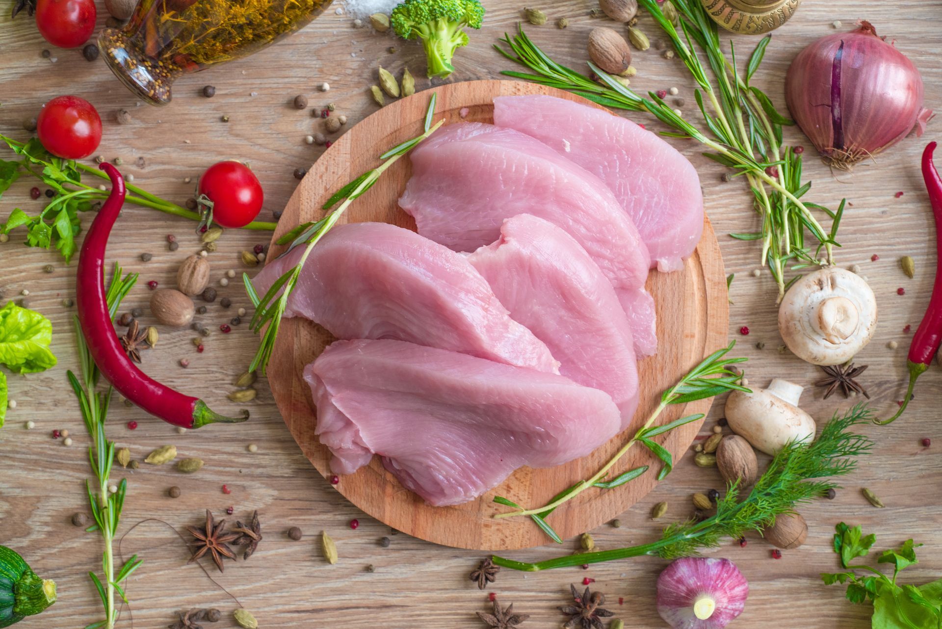Raw turkey breast slices on a wooden board, surrounded by herbs and vegetables.