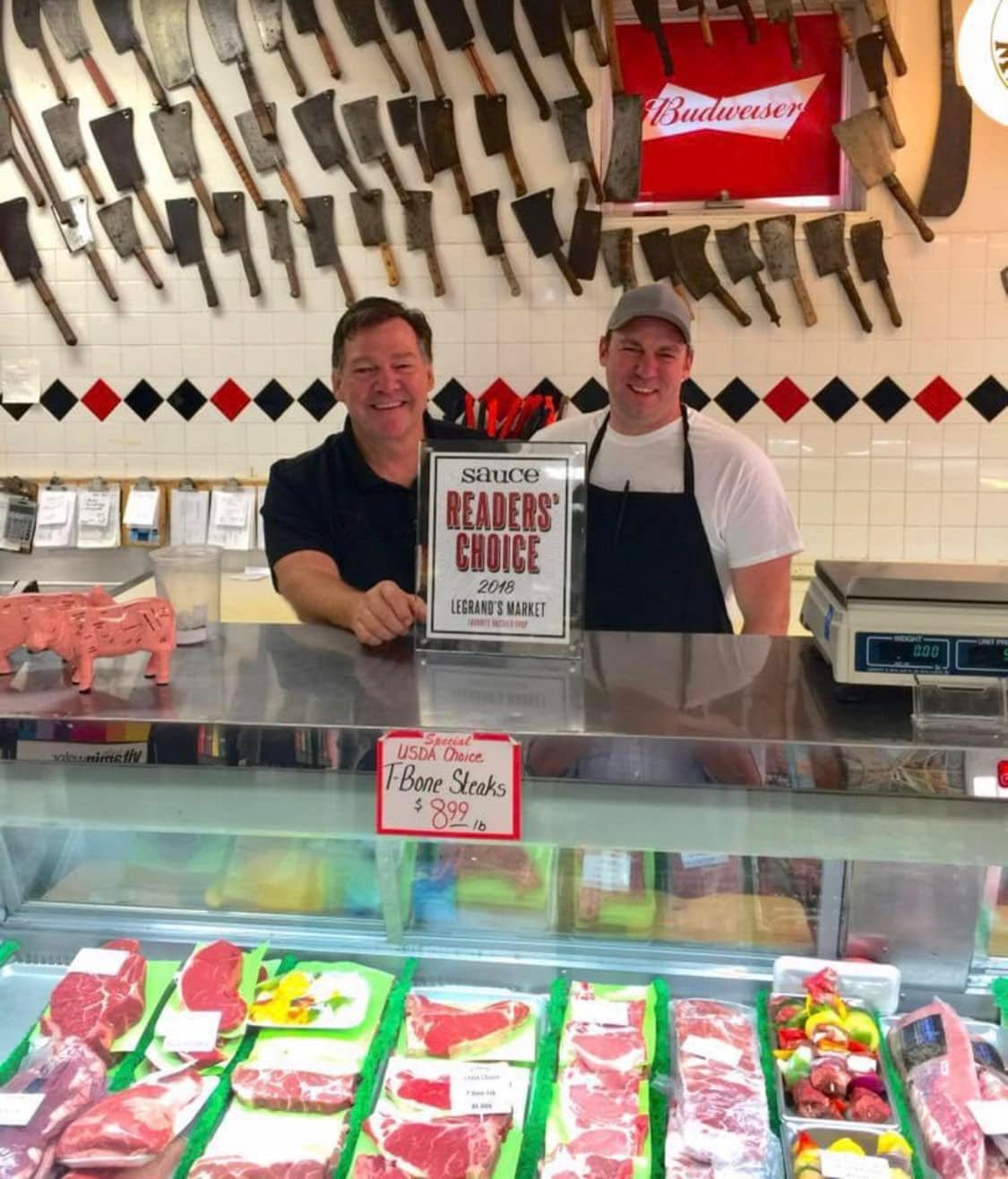 Two men behind a meat counter, smiling, with a 