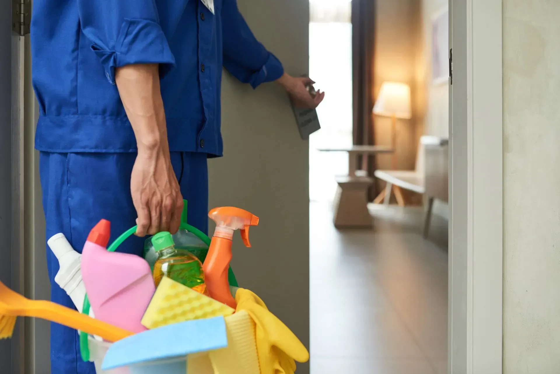 A man is carrying a bucket of cleaning supplies into a room.