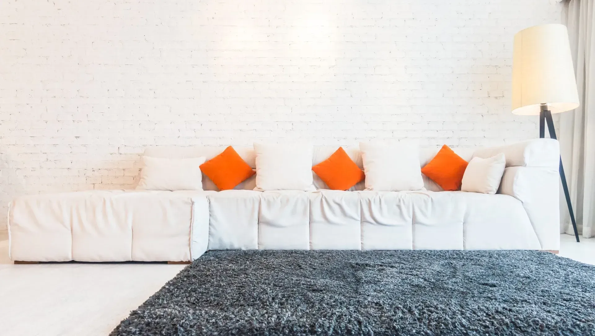 A living room with a white couch , orange pillows , and a black rug.