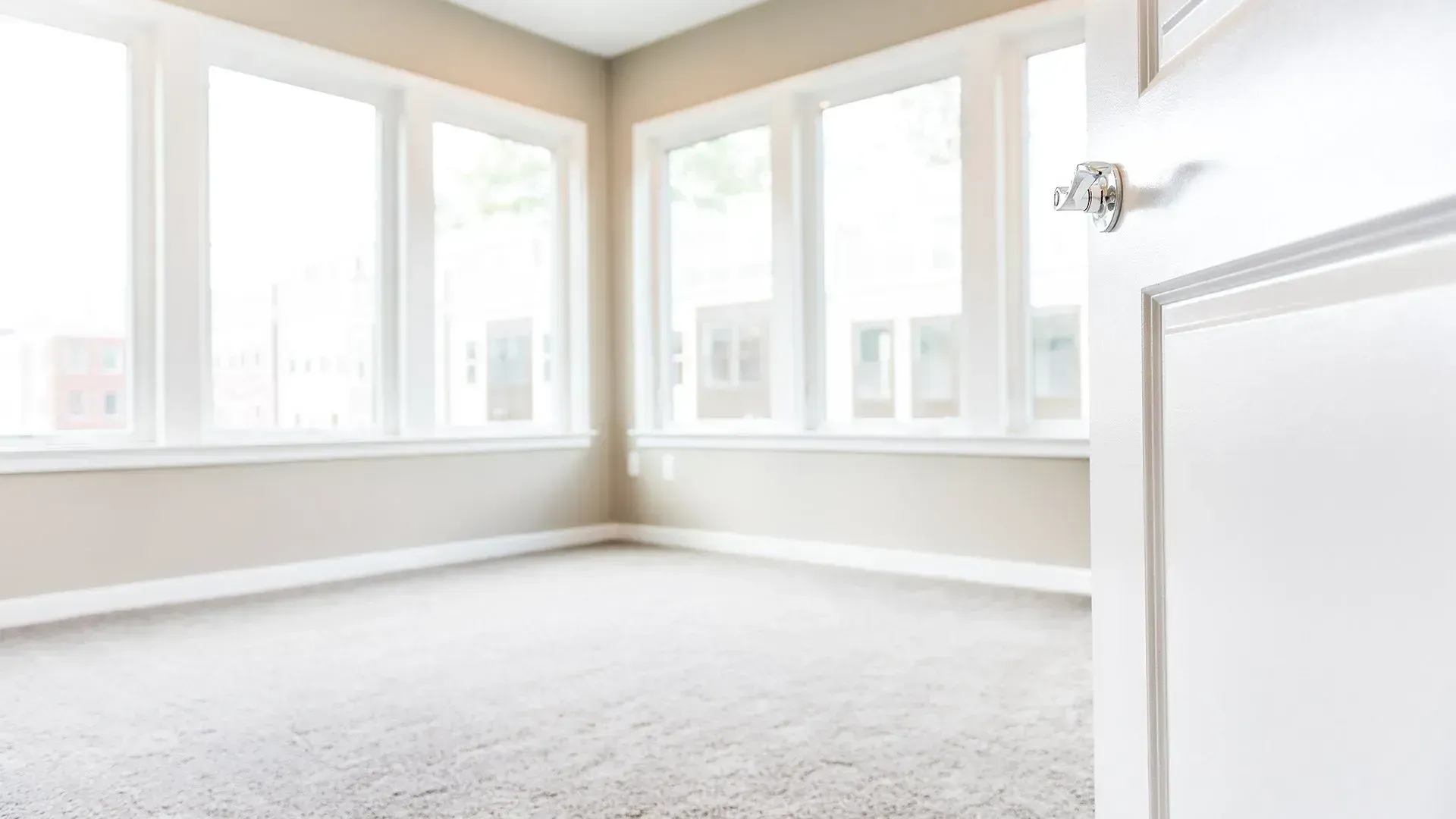 Bright empty room with beige walls, white trim, large windows, and carpeted floor.