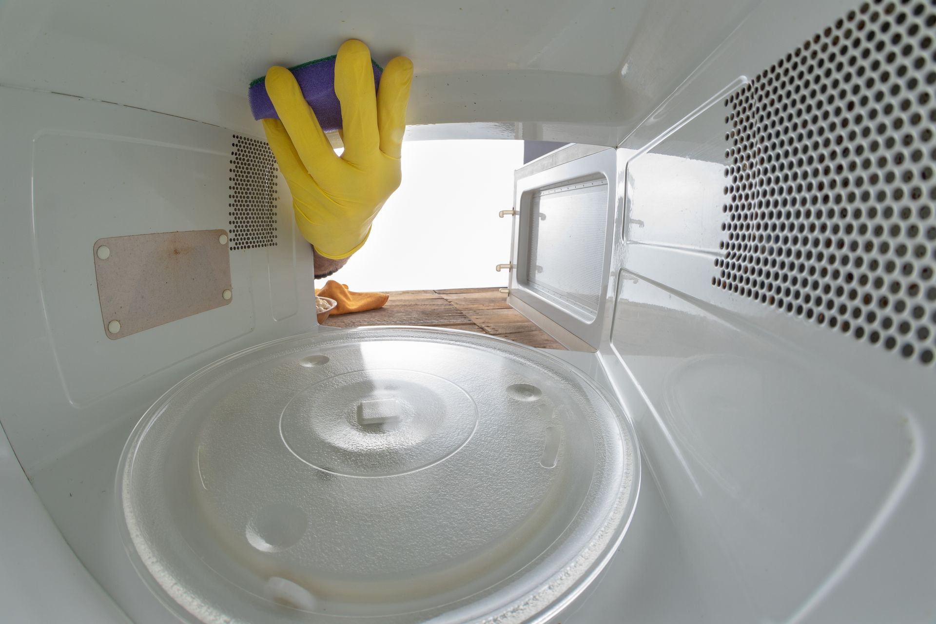 A person is cleaning a microwave with a sponge.