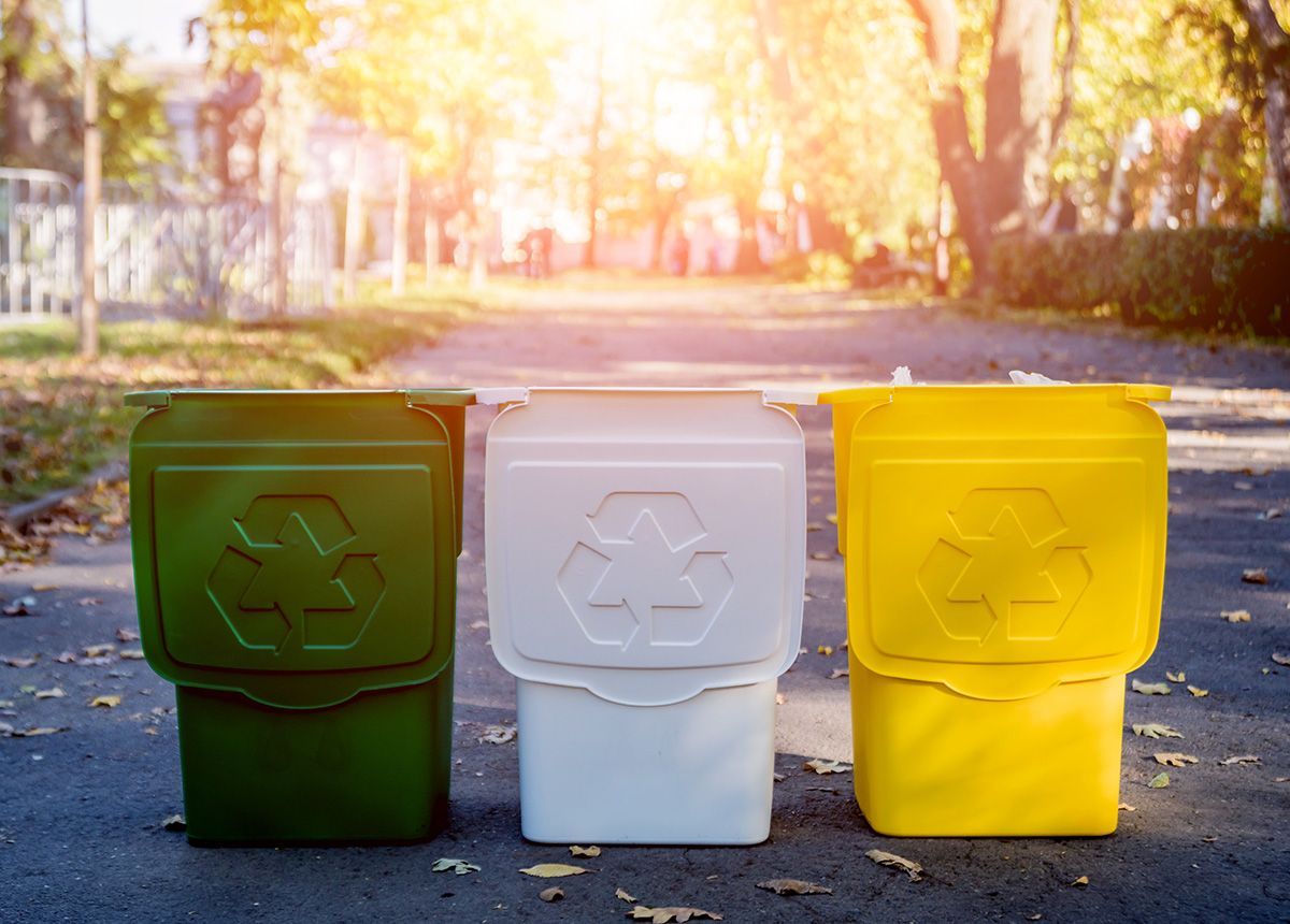 Three recycling bins are sitting next to each other on the side of a road.