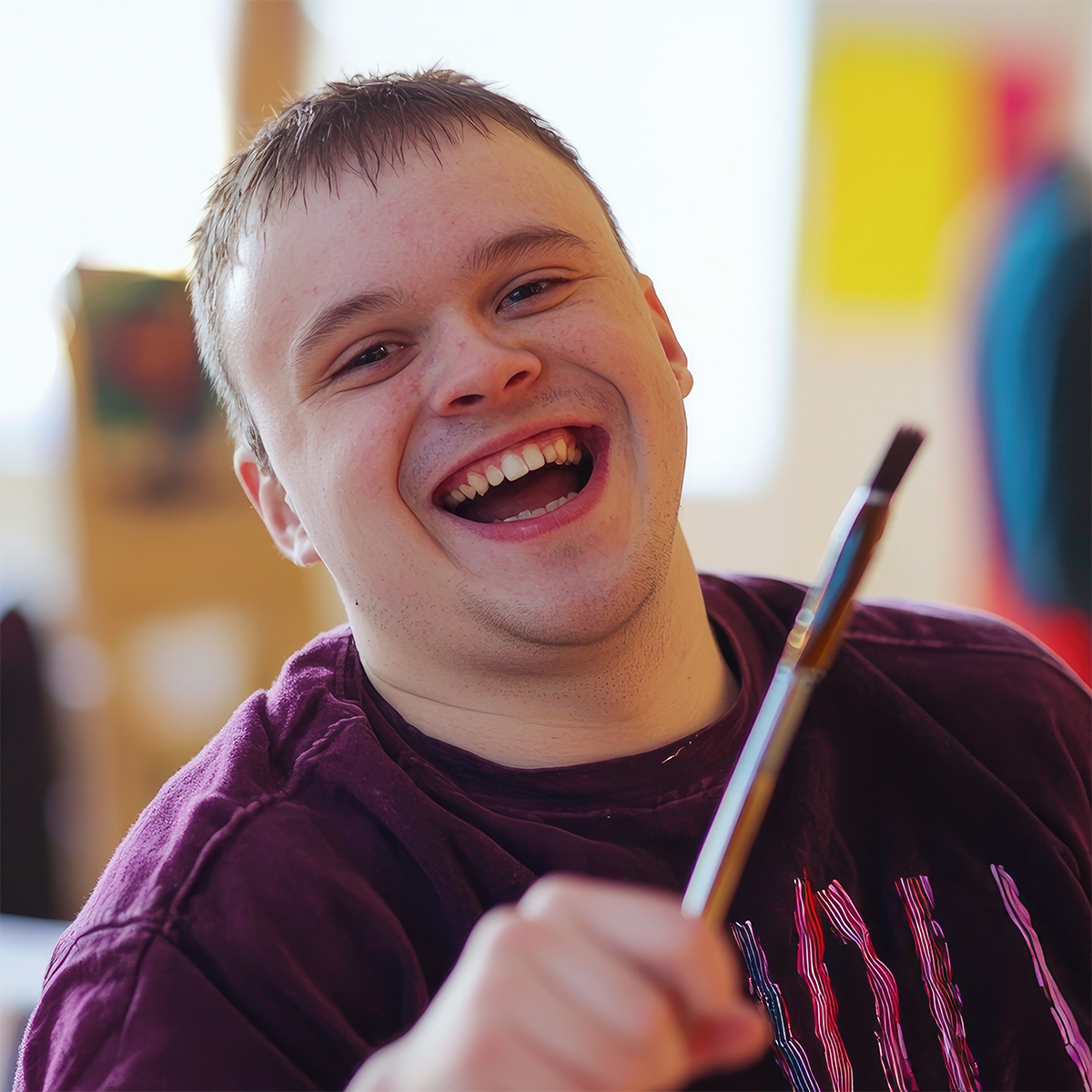 A man in a purple shirt is holding a brush and smiling