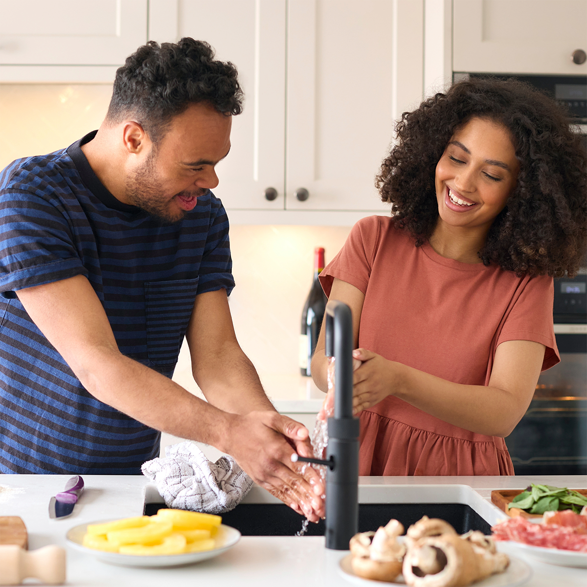 A man and a woman are washing their hands in a kitchen sink