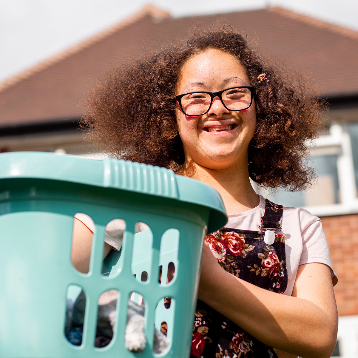 A young woman wearing glasses is holding a laundry basket.