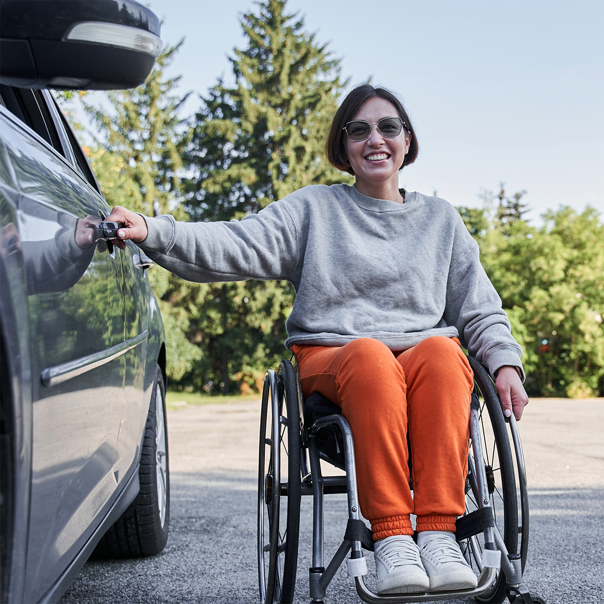 A woman in a wheelchair is sitting next to a car.