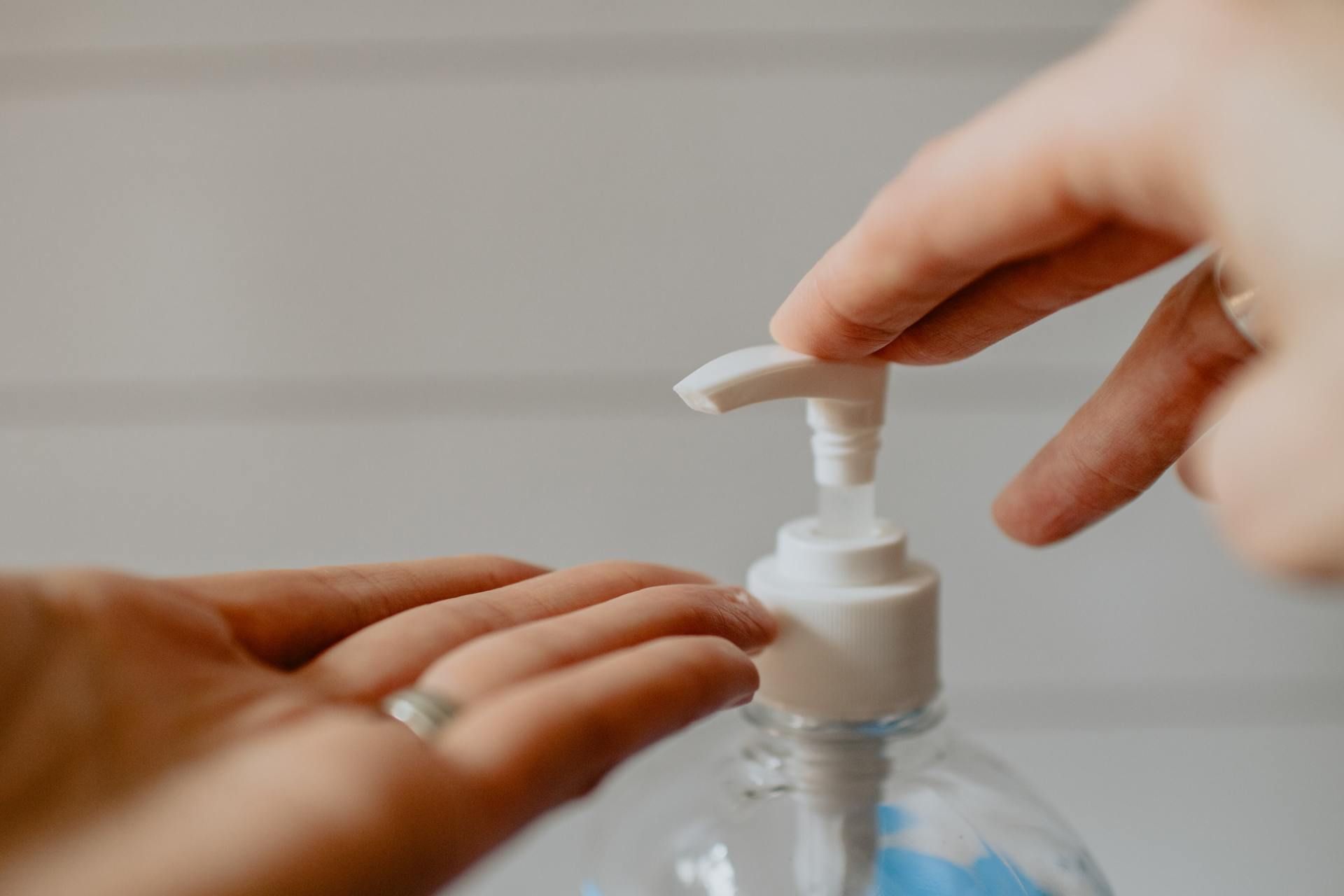 Hands using hand sanitizer pump over clear bottle