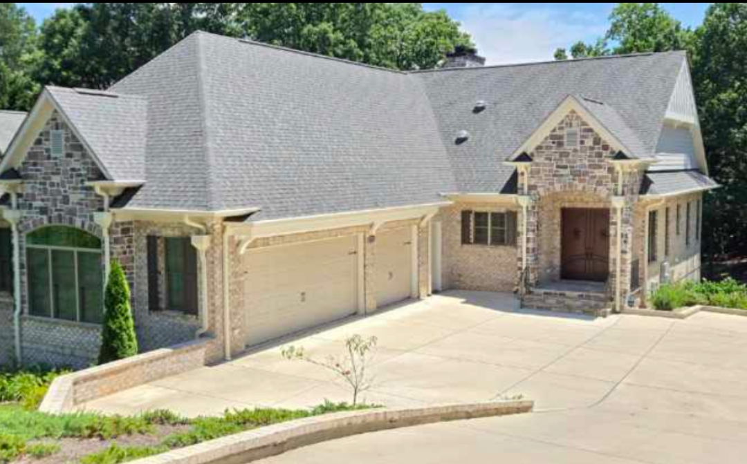 A large, light-colored house with a stone facade, garage, and driveway.