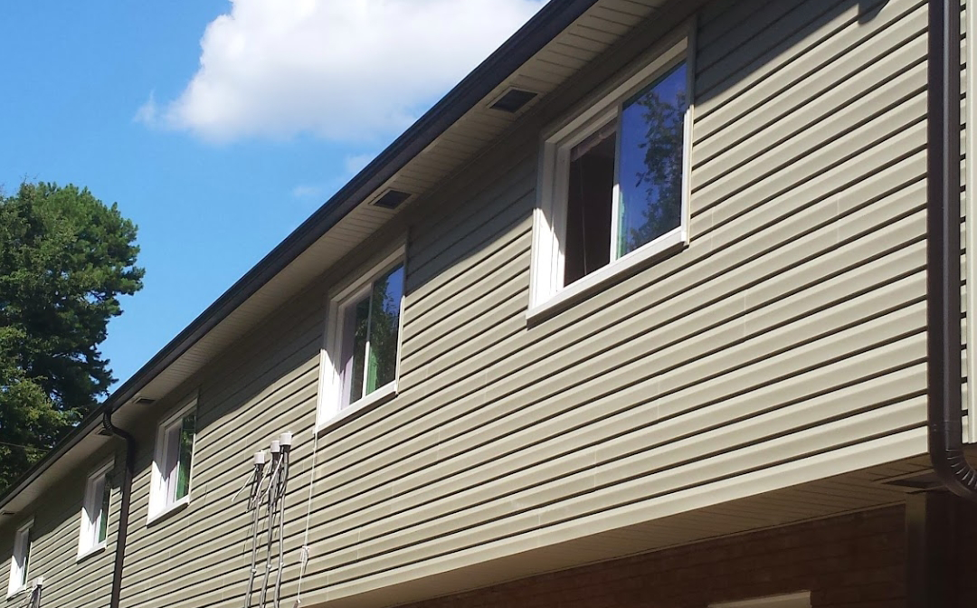 Building exterior with gray siding, white-framed windows, and brown trim against a blue sky with clouds.
