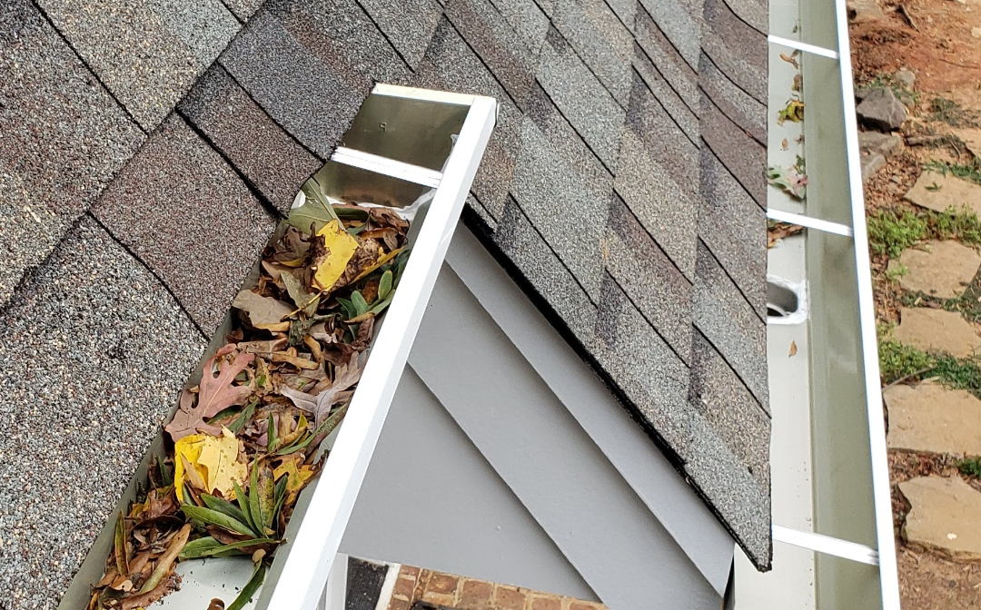 Gutter filled with leaves on a roof, illustrating a need for cleaning.