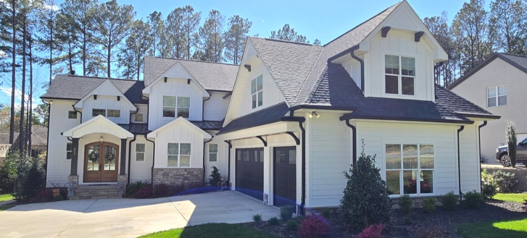 White house with black roof and trim, two-car garage, and stone accents.