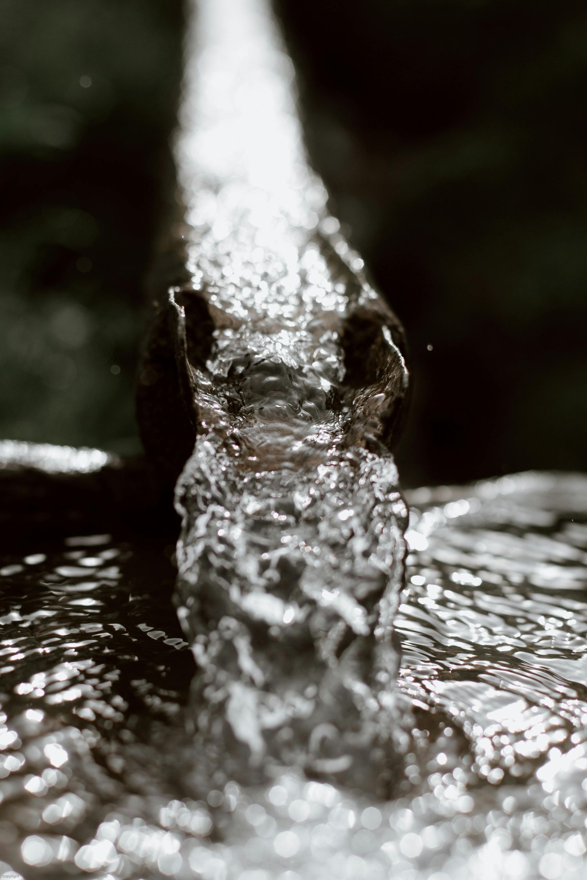 Water flowing from a faucet, close-up, dark background, liquid motion.