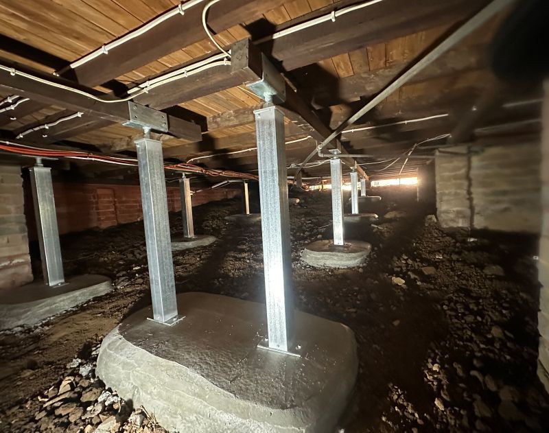 Crawlspace with support posts on concrete footings holding up wooden beams.