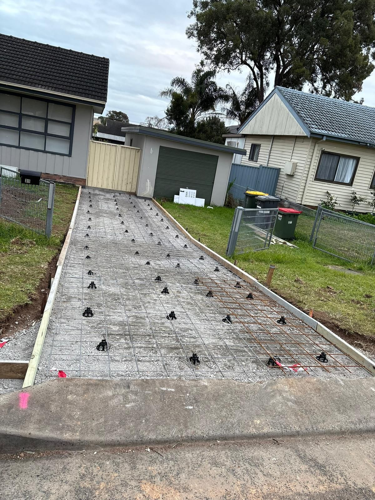 Driveway under construction with rebar and plastic supports, surrounded by houses and grass.