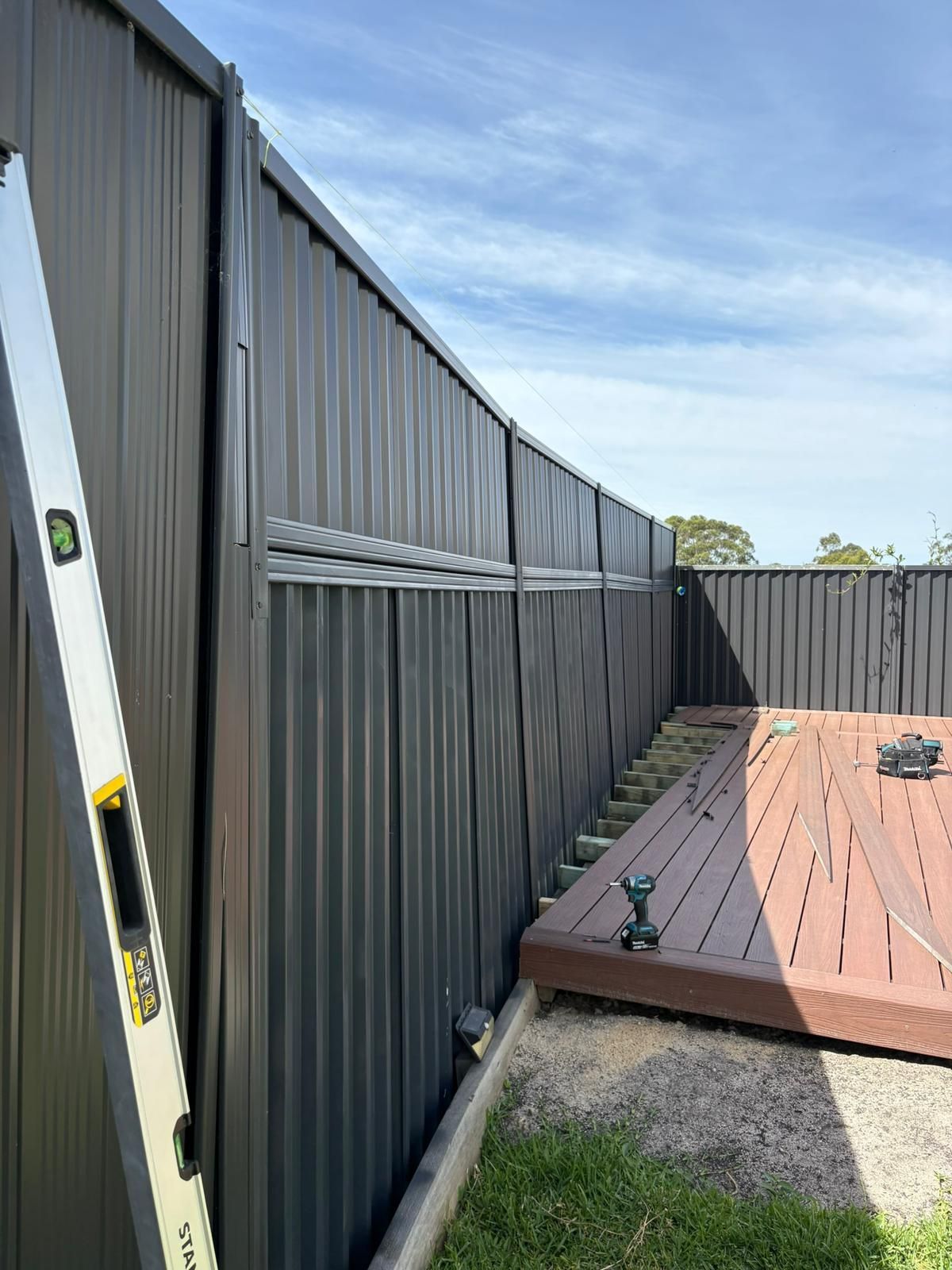 Black metal fence under construction; level leaning against it, deck visible.