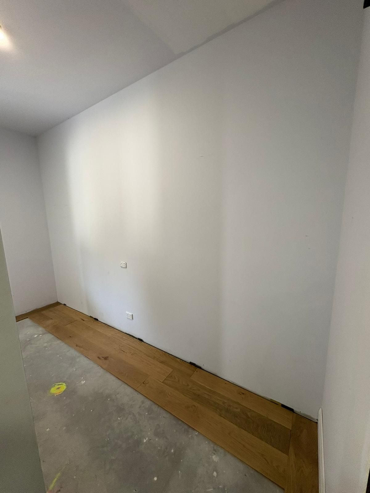 Empty room with white walls, wood flooring, and unfinished concrete floor.