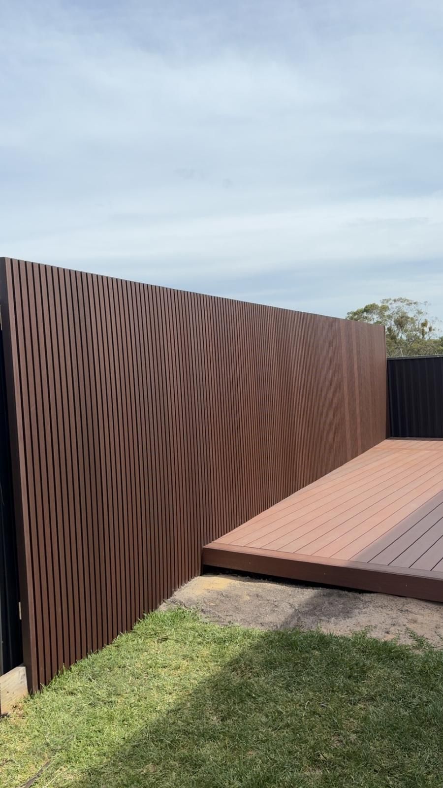 Brown decorative fence with a wood deck and green grass. Cloudy sky.
