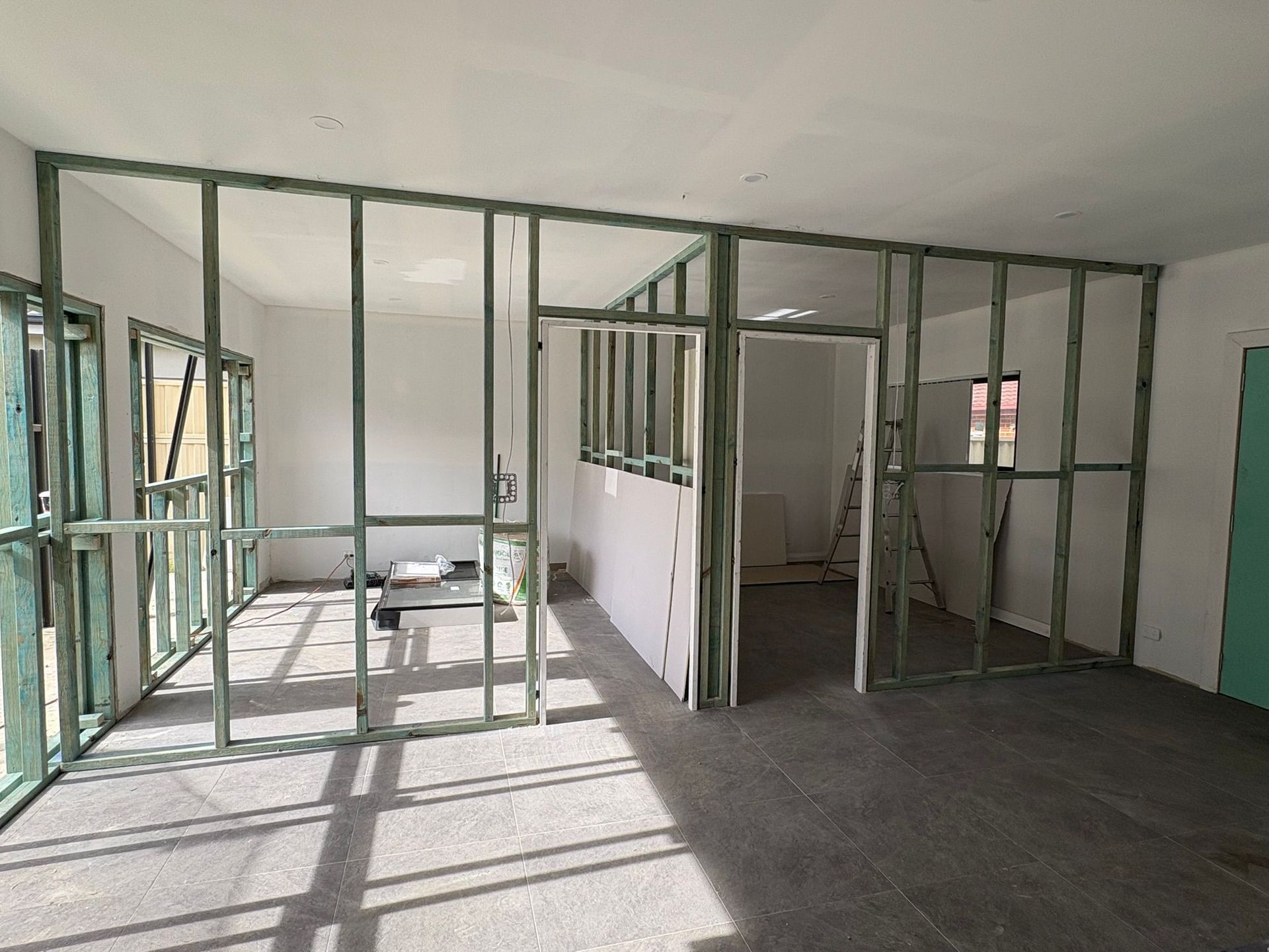 Interior framing of a room under construction with green wood studs and partial drywall.