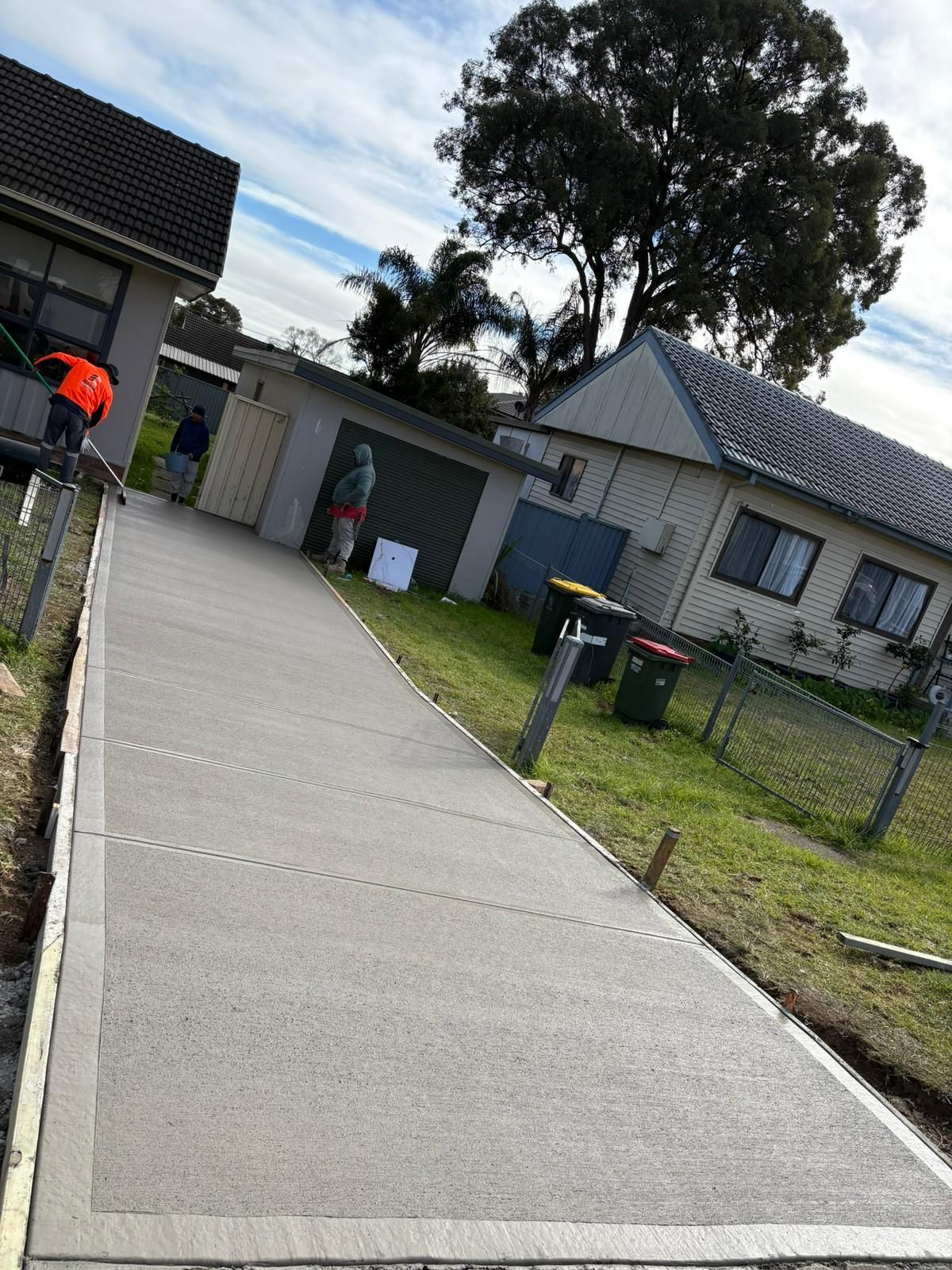 A newly poured concrete path with people in the background, set in a residential area.