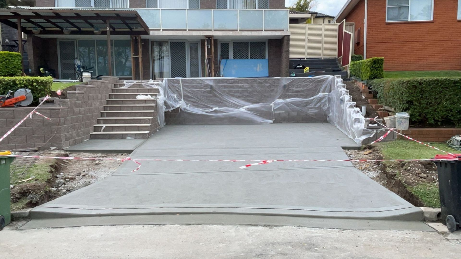 Newly poured concrete driveway with steps leading up to a house; partially covered in plastic.