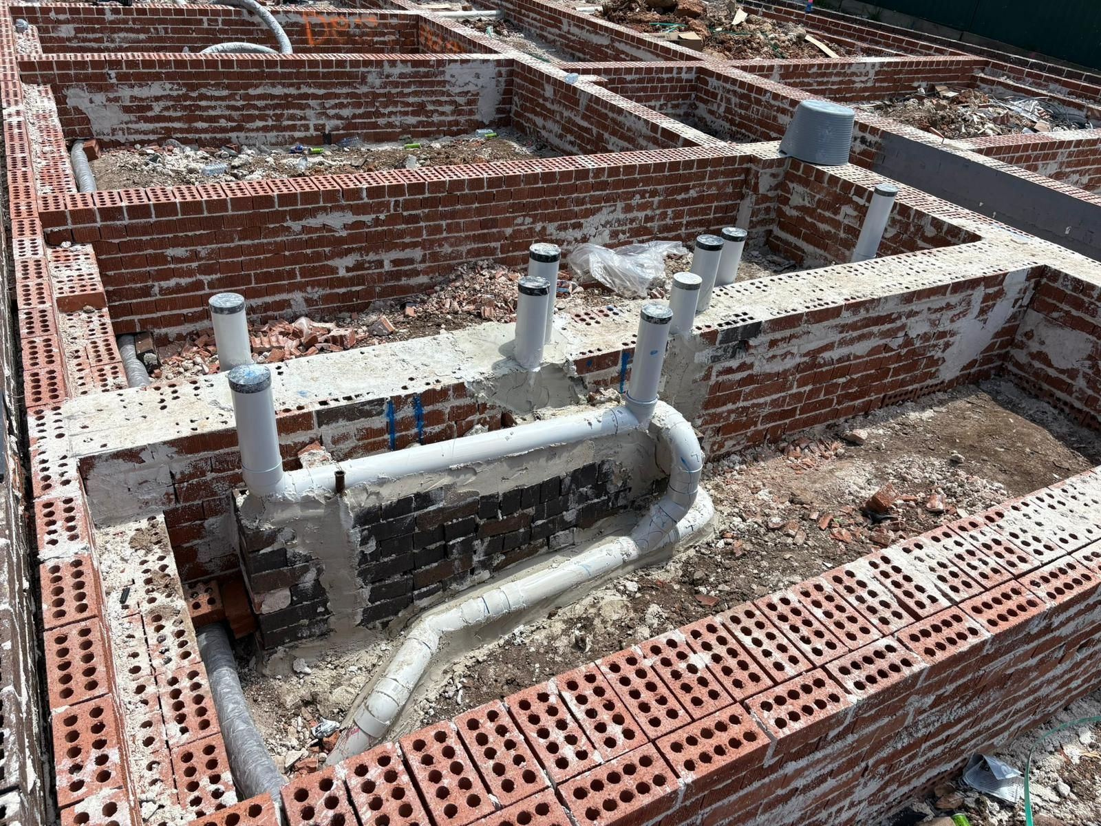 Brick foundation under construction with plumbing pipes protruding.
