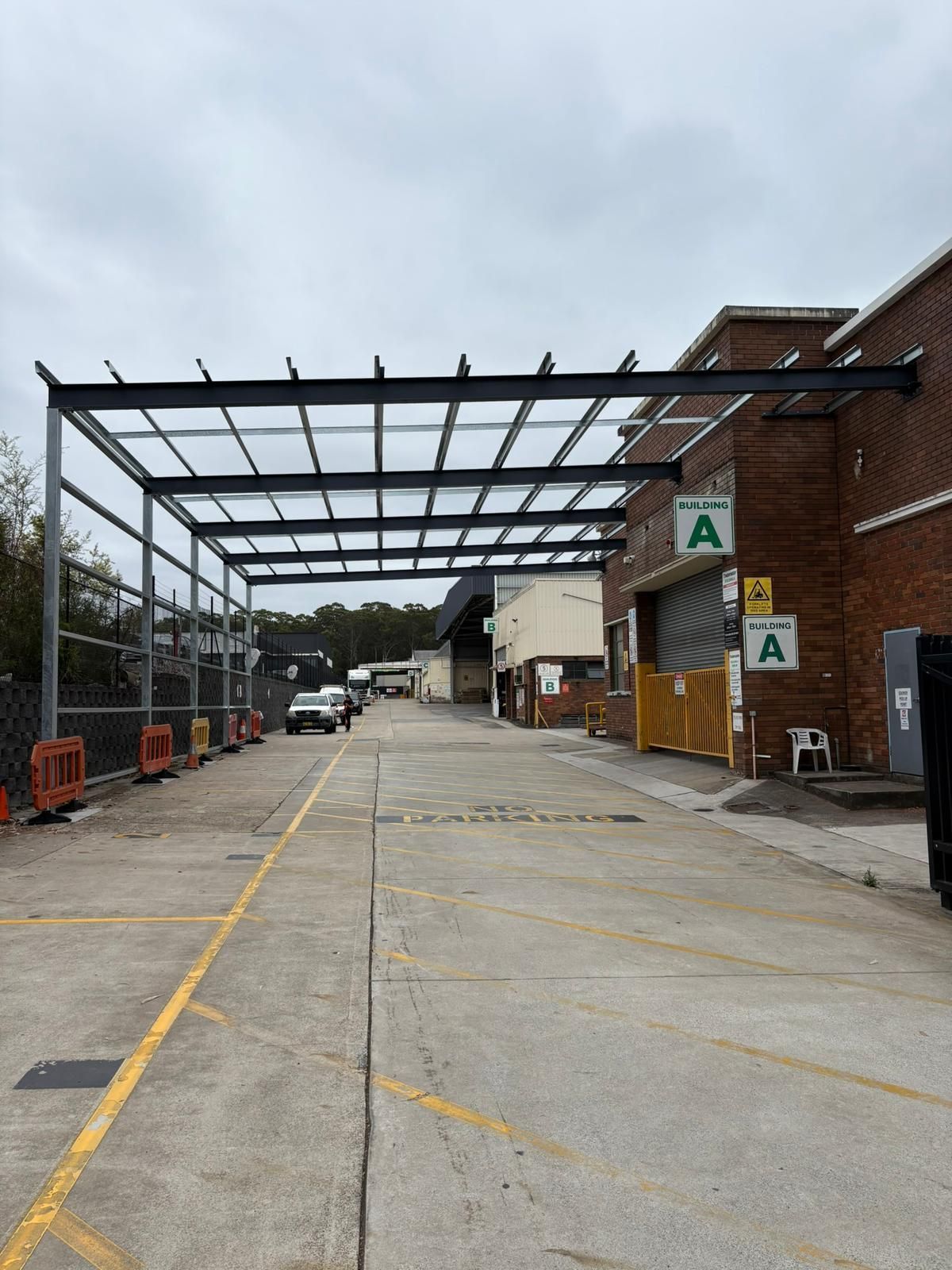 Metal framed awning over a concrete driveway, next to a brick building.