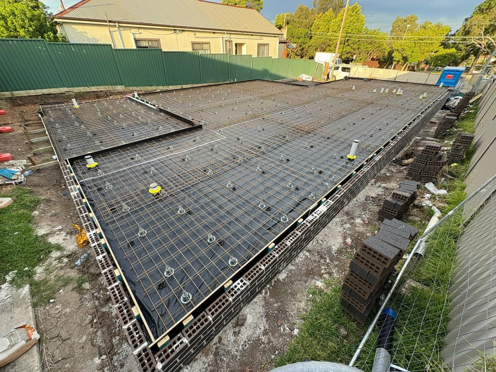 Construction site with prepared foundation for a building; rebar, formwork, and utilities visible.