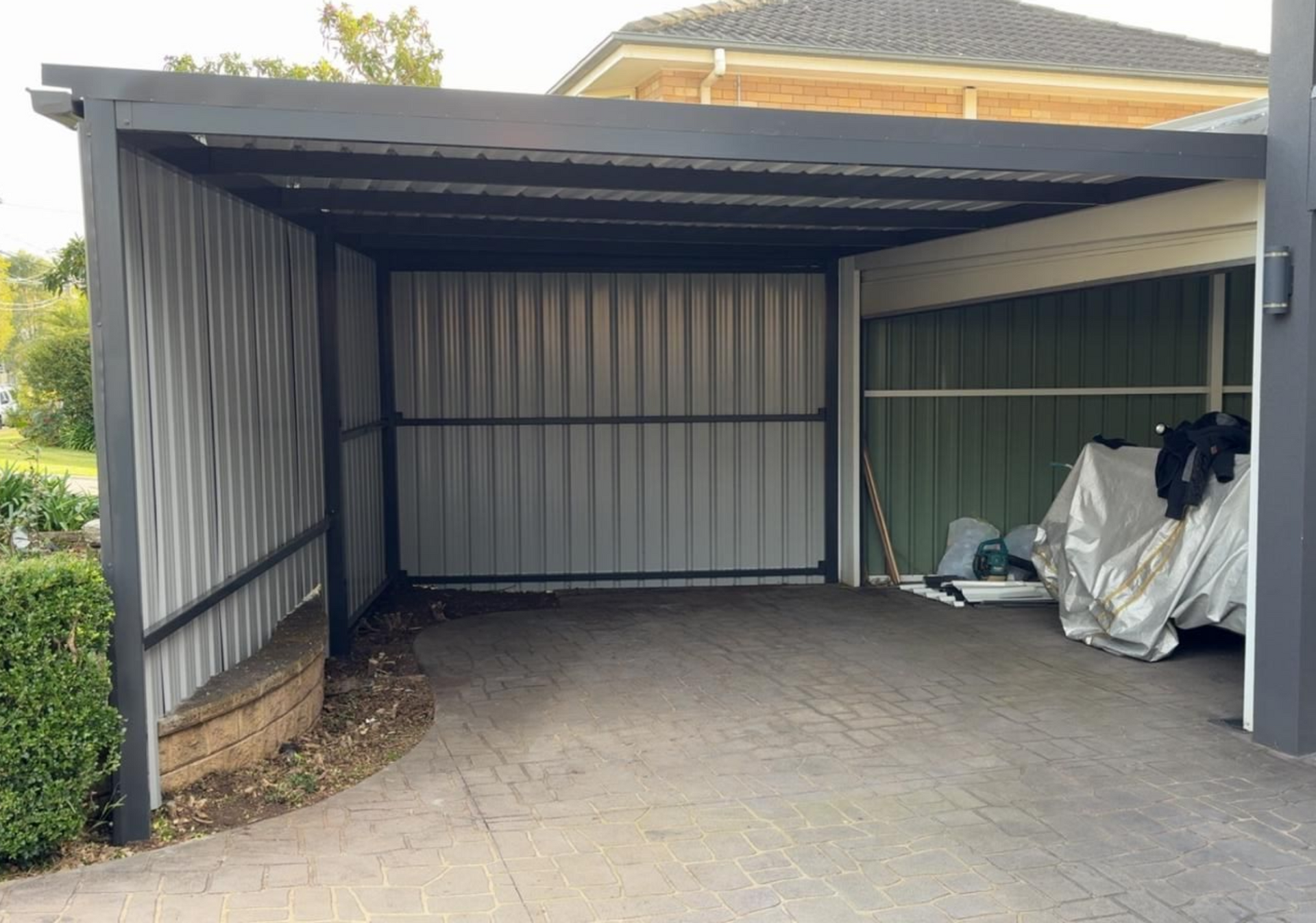 Open carport with gray corrugated metal walls and roof, on a concrete driveway.