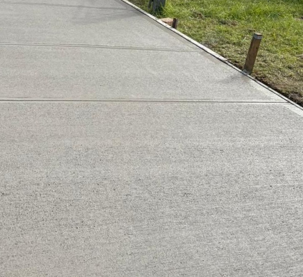 A person using a floor scraper to spread wet, light-colored concrete on a floor.