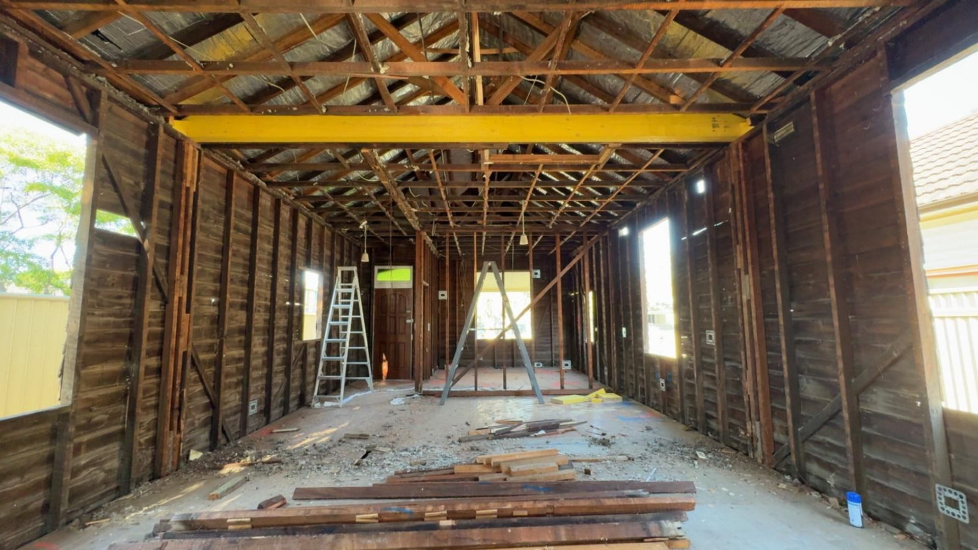 Interior view of a wooden structure undergoing renovation, showing exposed beams, walls, and scattered debris.