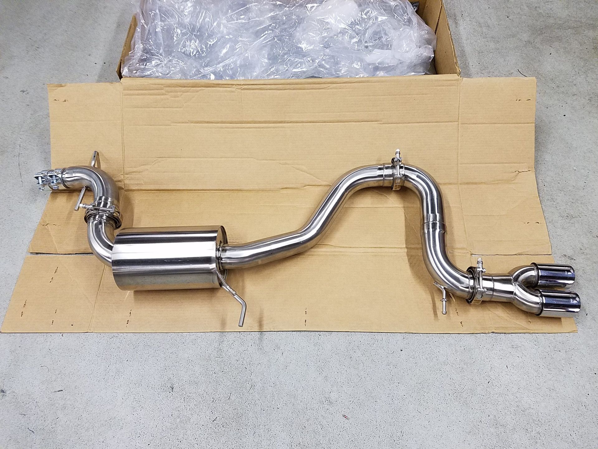 Stainless steel car exhaust system laid out on a cardboard box. | Autobahn Performance Inc