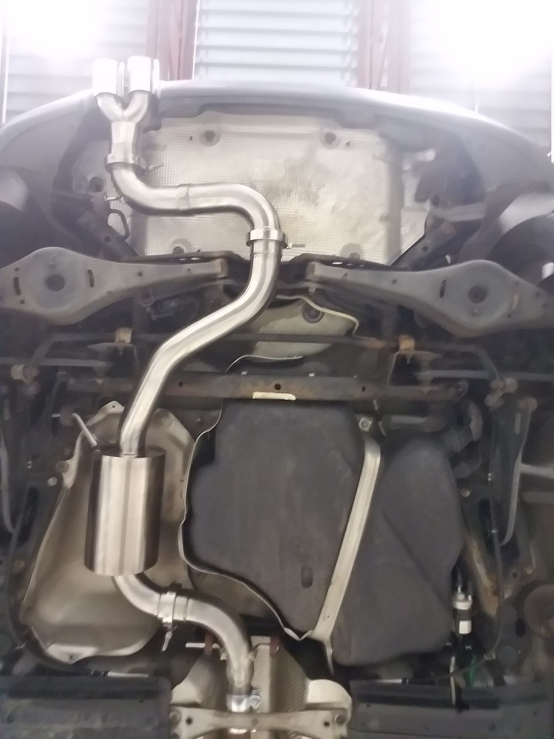 Underside view of a car showing a custom exhaust system in silver metal. | Autobahn Performance Inc