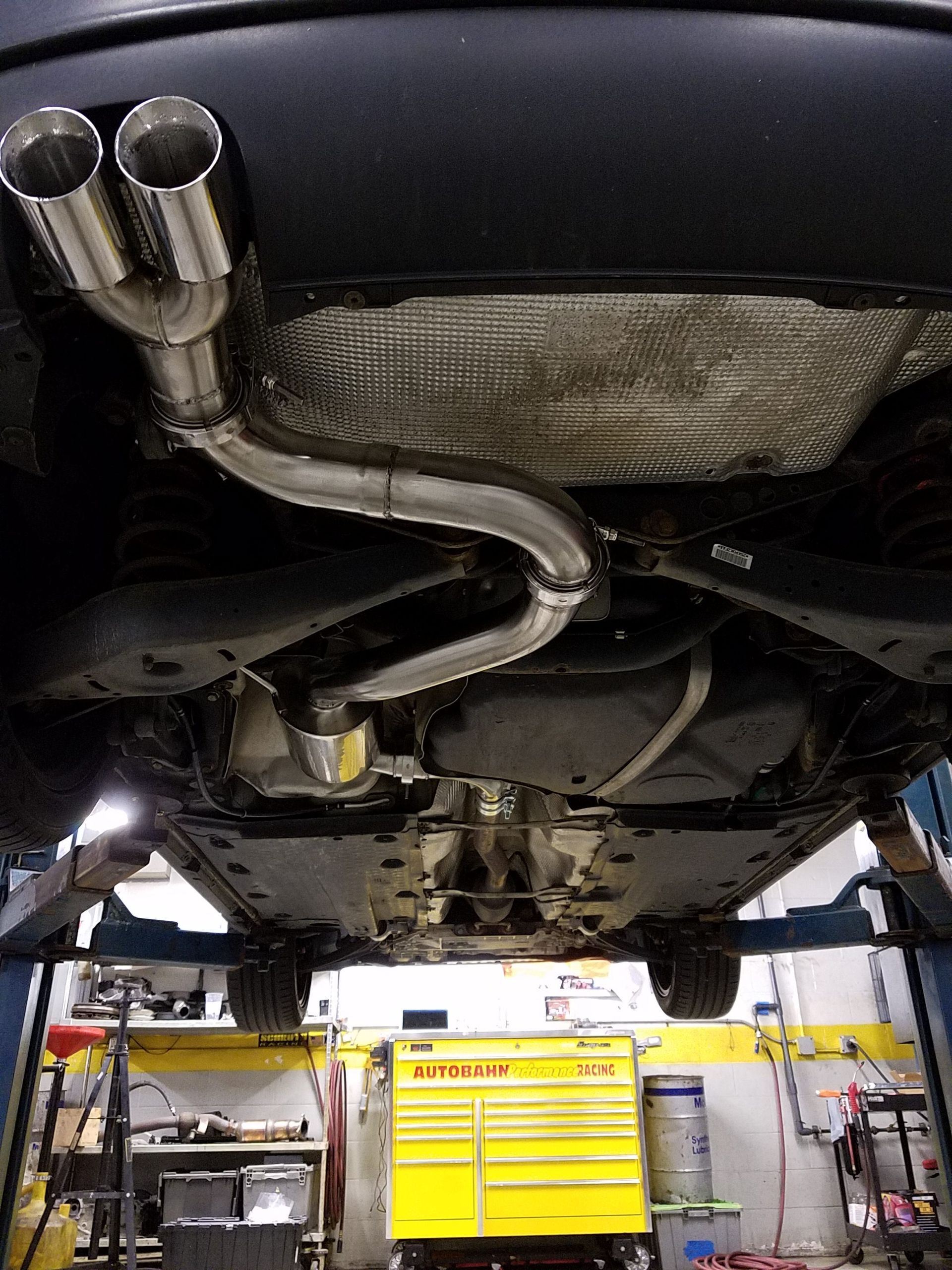 Car on a lift with a new, shiny, dual-tip exhaust system installed, visible from underneath. | Autobahn Performance Inc