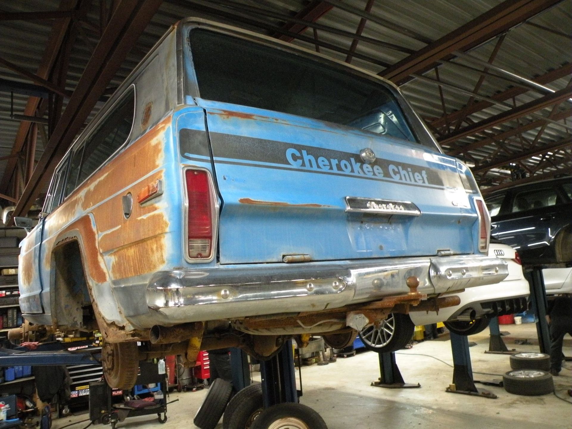 Rear view of a rusty blue Jeep Cherokee Chief on a lift in a garage. | Autobahn Performance Inc