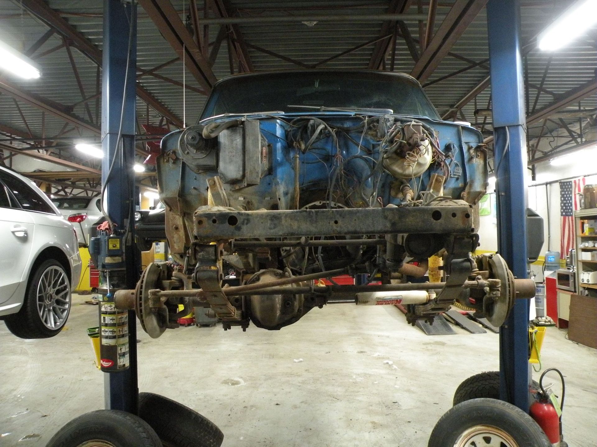A blue truck, on a lift, undergoing repair. Front end disassembled in a garage setting. | Autobahn Performance Inc