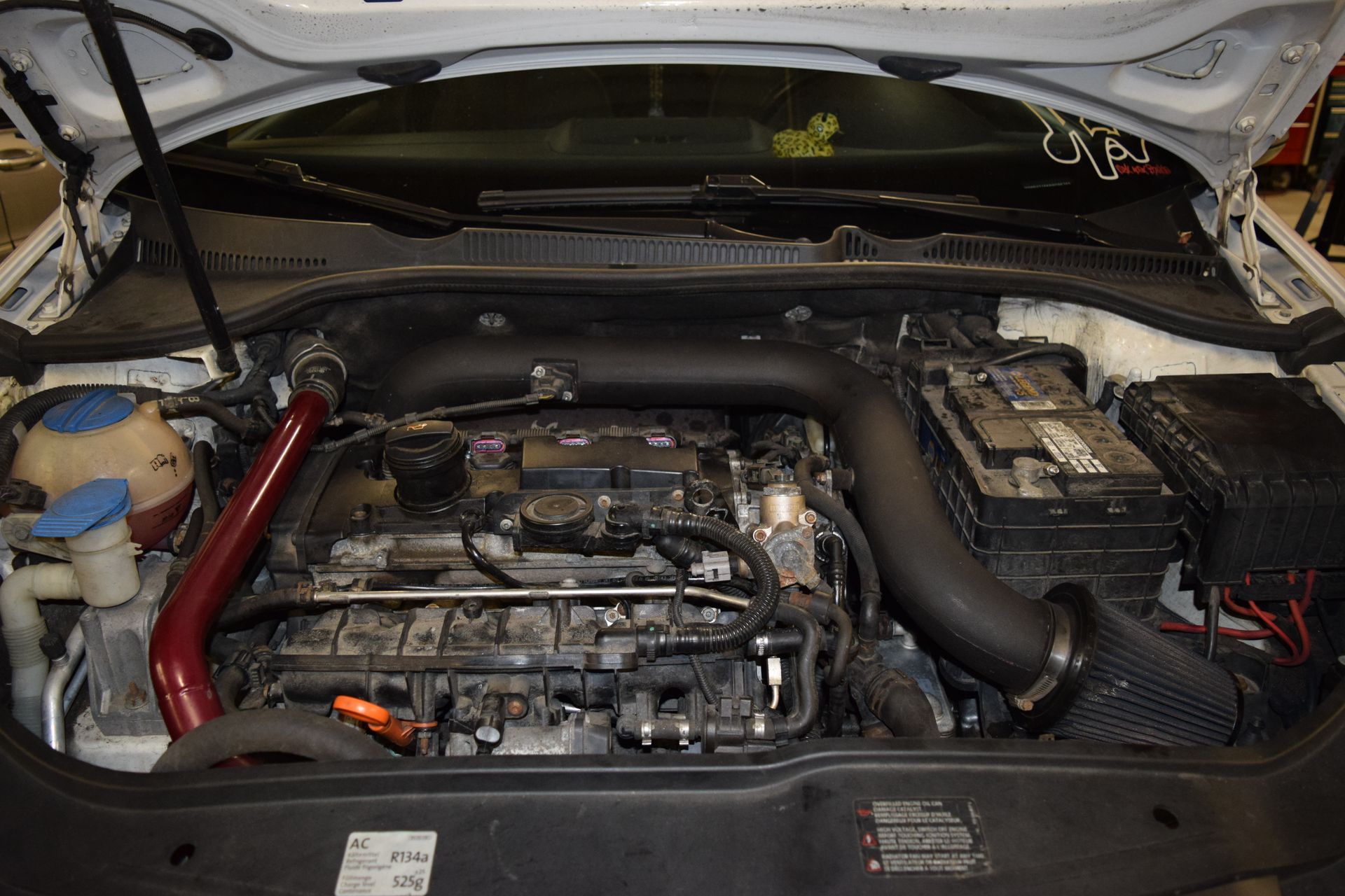 Open car hood revealing a car engine with a black intake tube and red piping. | Autobahn Performance Inc