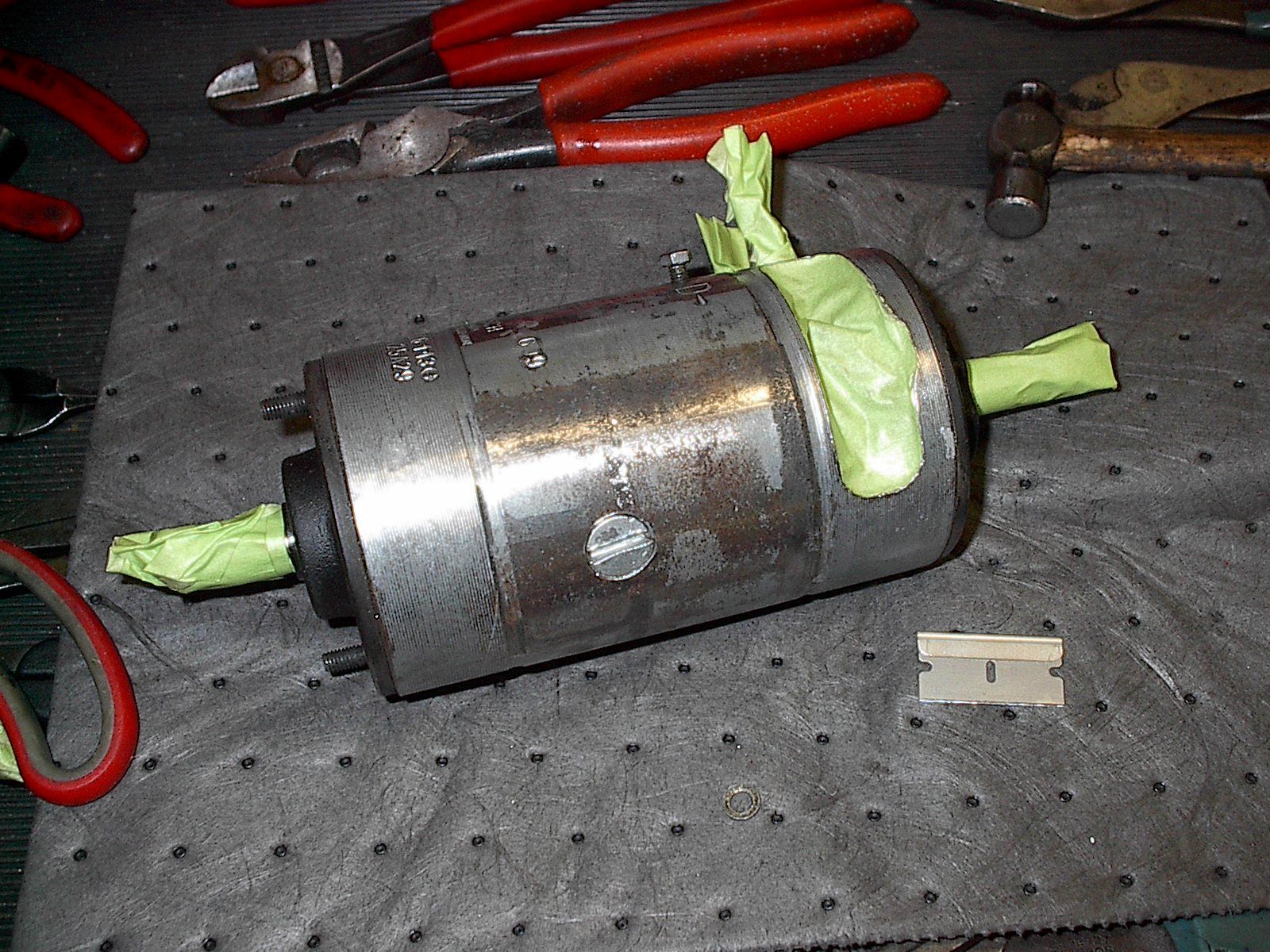 A cylindrical metal object with green tape on ends, tools on a dark textured surface. | Autobahn Performance Inc