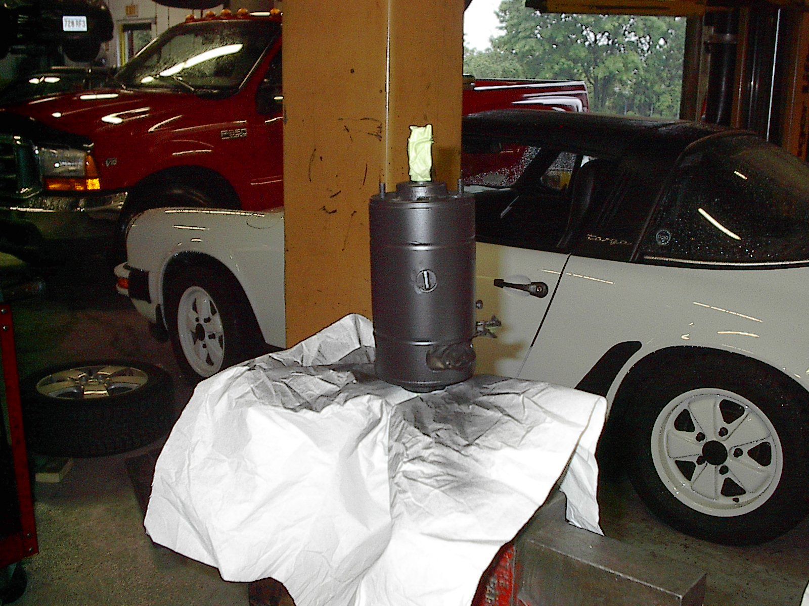 Black painted cylinder on a white cloth in a garage, with a white Porsche and red truck in the background. | Autobahn Performance Inc