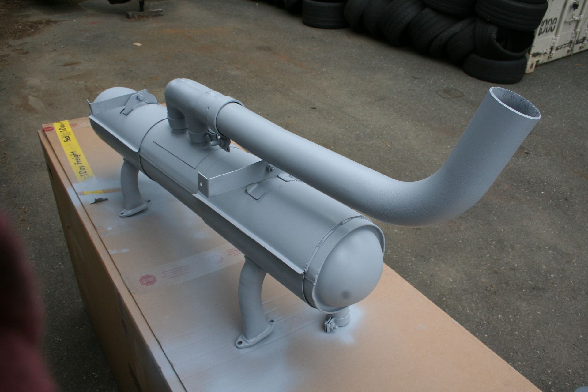 Grey-painted metal industrial exhaust system on a tan cardboard surface. | Autobahn Performance Inc