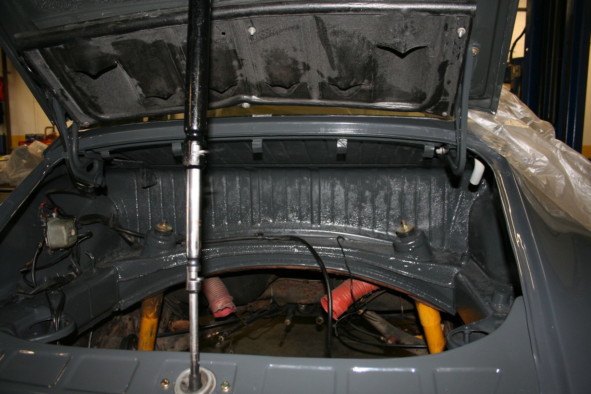 Open trunk of a gray car interior, showing the engine compartment with various parts, and a support rod. | Autobahn Performance Inc
